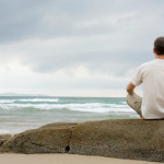 Man meditating on a rock at the sea